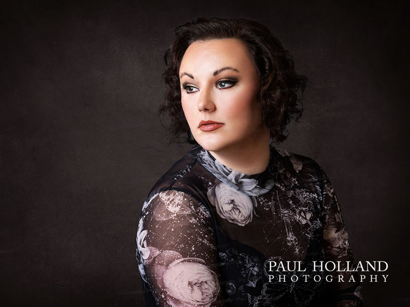 Portrait of a woman with short dark curls in a floral top, looking to the side against a dark textured background.